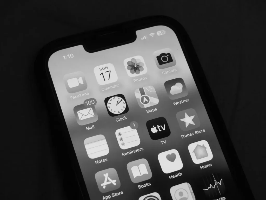 Mains tenant un smartphone affichant l'interface iOS avec widgets adaptatifs et contrôles simplifiés