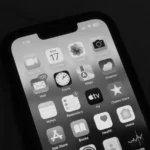 Mains tenant un smartphone affichant l'interface iOS avec widgets adaptatifs et contrôles simplifiés