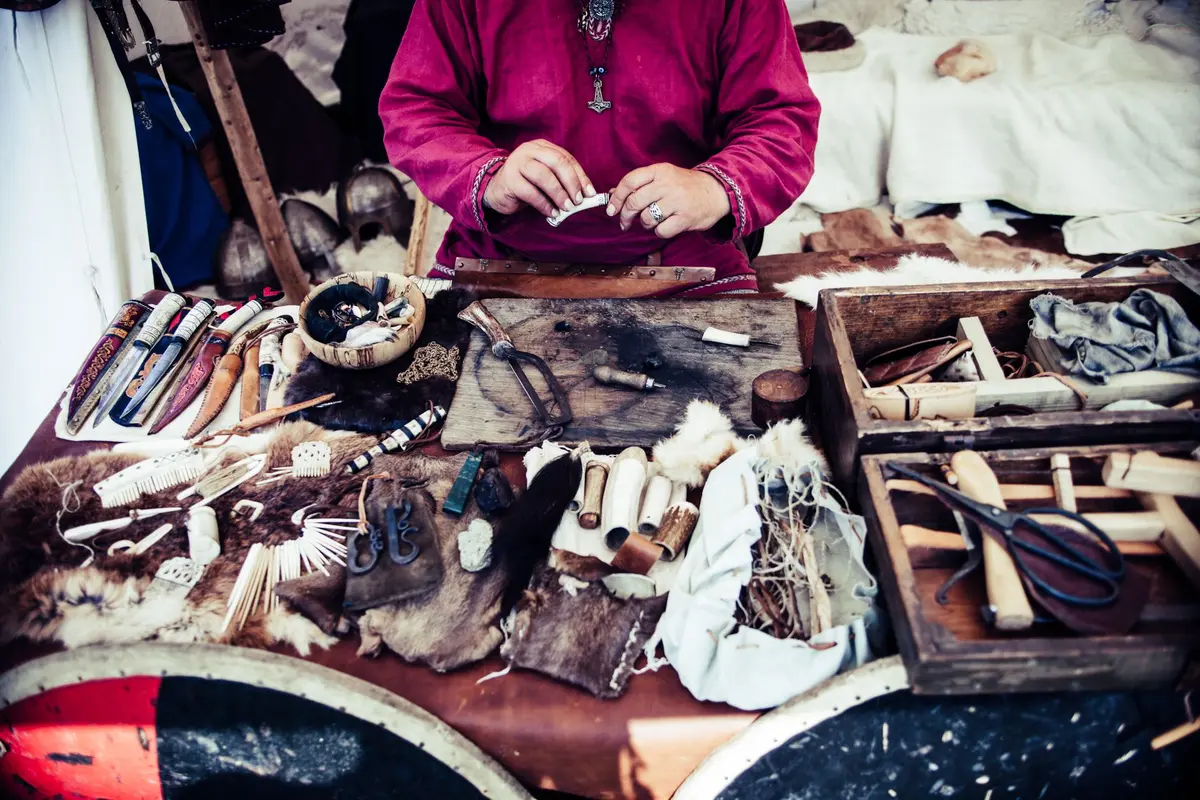 Établis de menuiserie et forge dans un atelier médiéval avec ressources et outils.