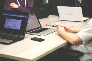 Mains anonymes tapant sur un ordinateur portable sur un bureau en plein jour, carnet et stylo à côté