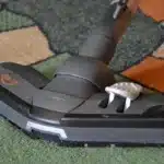 Robot aspirateur noir en train de s'accrocher à sa station de vidage blanche dans un salon lumineux