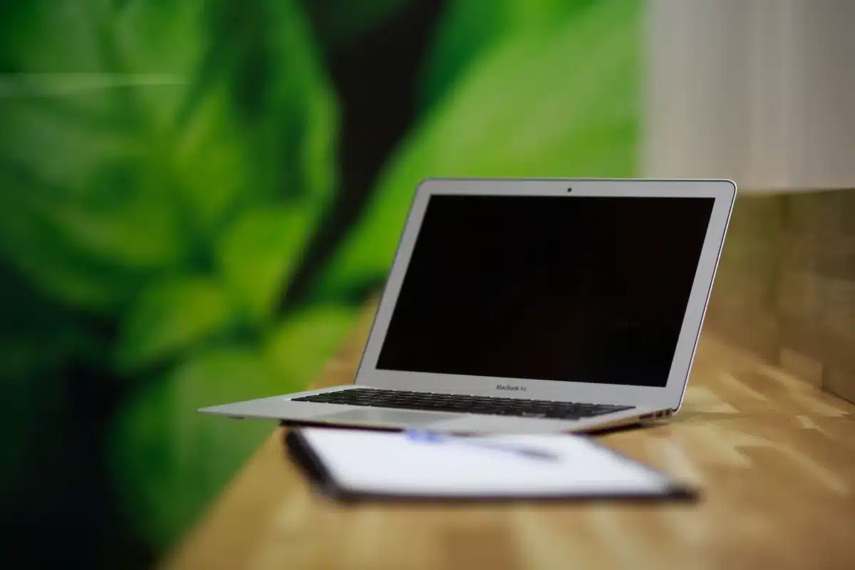close-up of anonymous hands typing on a laptop keyboard with an abstract glowing waveform on the screen, an office notepad and pen beside it