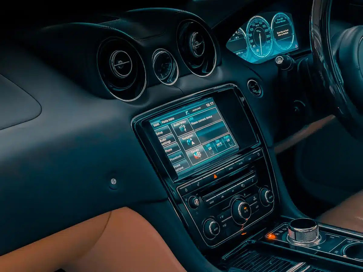 Bright interior shot of a car centre console with an anonymous infotainment screen showing generic app icons, a blurred smartphone lying beside it