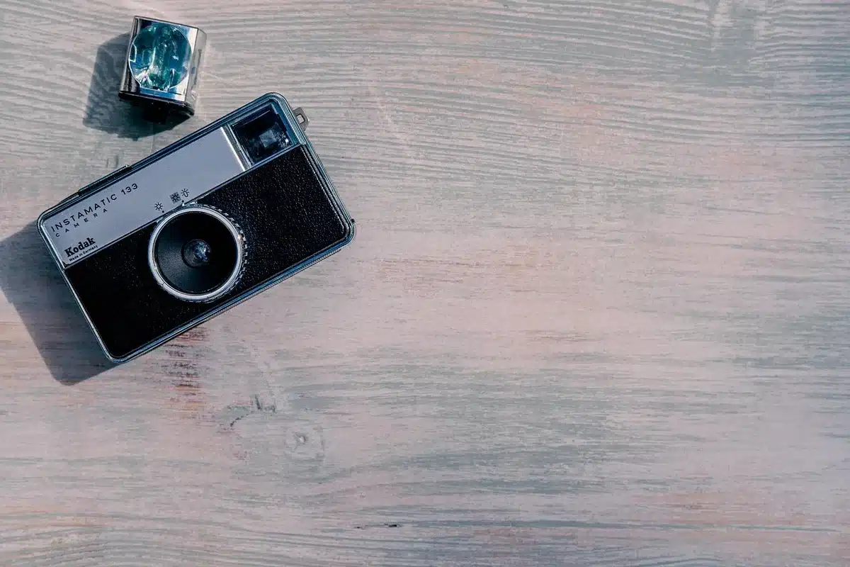 A compact unbranded camera resting on a wooden desk with an open notebook and a pen, daylight from a window, clean everyday scene