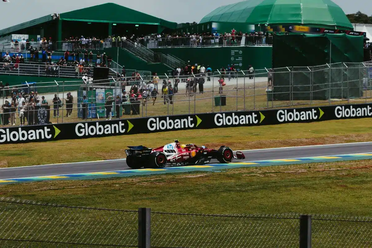 Wide shot of a race paddock at daytime with an empty grid, tire stacks and a covered bike under a canopy, preparation activity hinting at an upcoming race