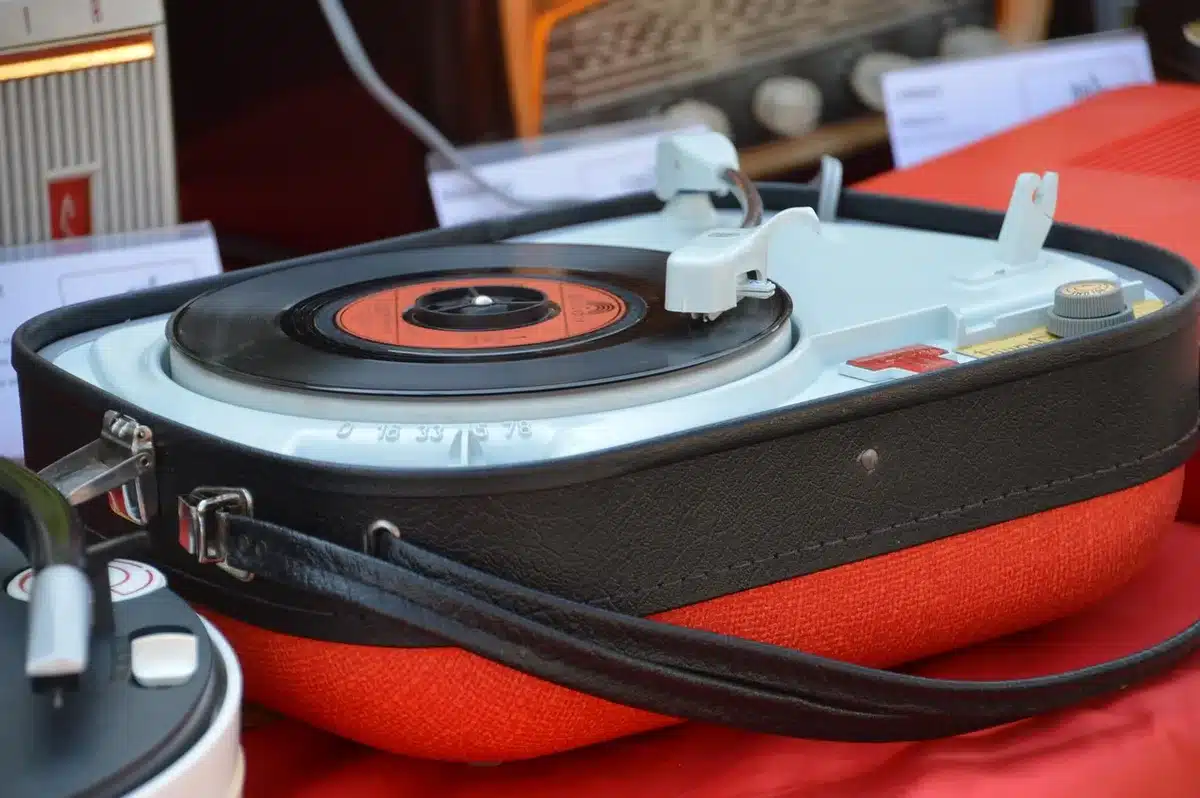 Close-up of hands adjusting a small silver phono preamp knob on a wooden table, with a blurred record sleeve in the background