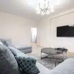 Télécommande moderne posée sur une table basse devant une TV allumée en plein jour
