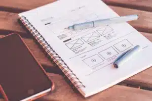 Bureau lumineux près d'une fenêtre avec un smartphone générique, un objectif et un carnet